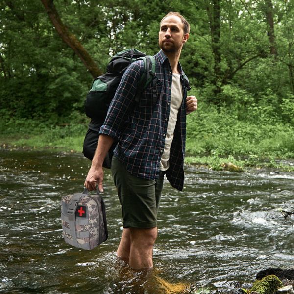 Camper walking through stream with health kit in one hand and a packed backpack in the other observing nature around him